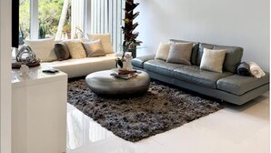 Ein modernes Wohnzimmer mit Deckenventilator, einem grauen Sofa, einem weißen Couchtisch und großen Fenstern.