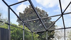 Eine moderne Außenpatio mit einem geometrischen Metallgestell, einem Sitzbereich und Blick auf einen Garten mit Bäumen und Pflanzen.
