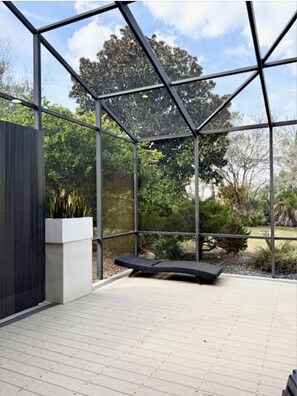Eine moderne Außenpatio mit einem geometrischen Metallgestell, einem Sitzbereich und Blick auf einen Garten mit Bäumen und Pflanzen.
