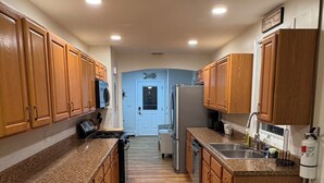 A kitchen with wooden cabinets, granite countertops, a stainless steel refrigerator, and a microwave. - Shore House, Beach + Boardwalk, Parking for 7, Point Pleasant Beach (Point Pleasant Beach)