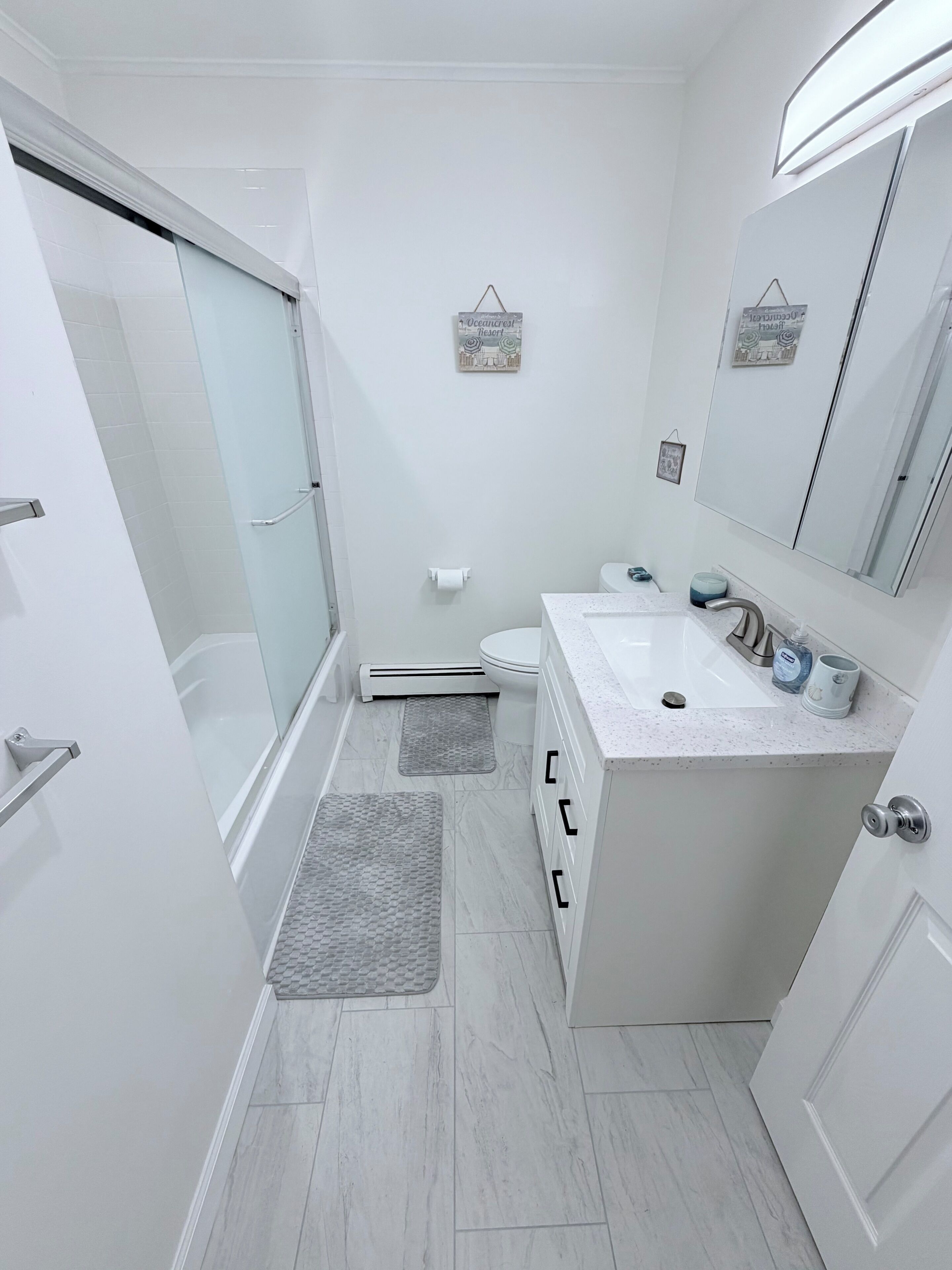 Un baño moderno con cabina de ducha de vidrio, un lavabo blanco y encimera de mármol, y un espejo grande.
