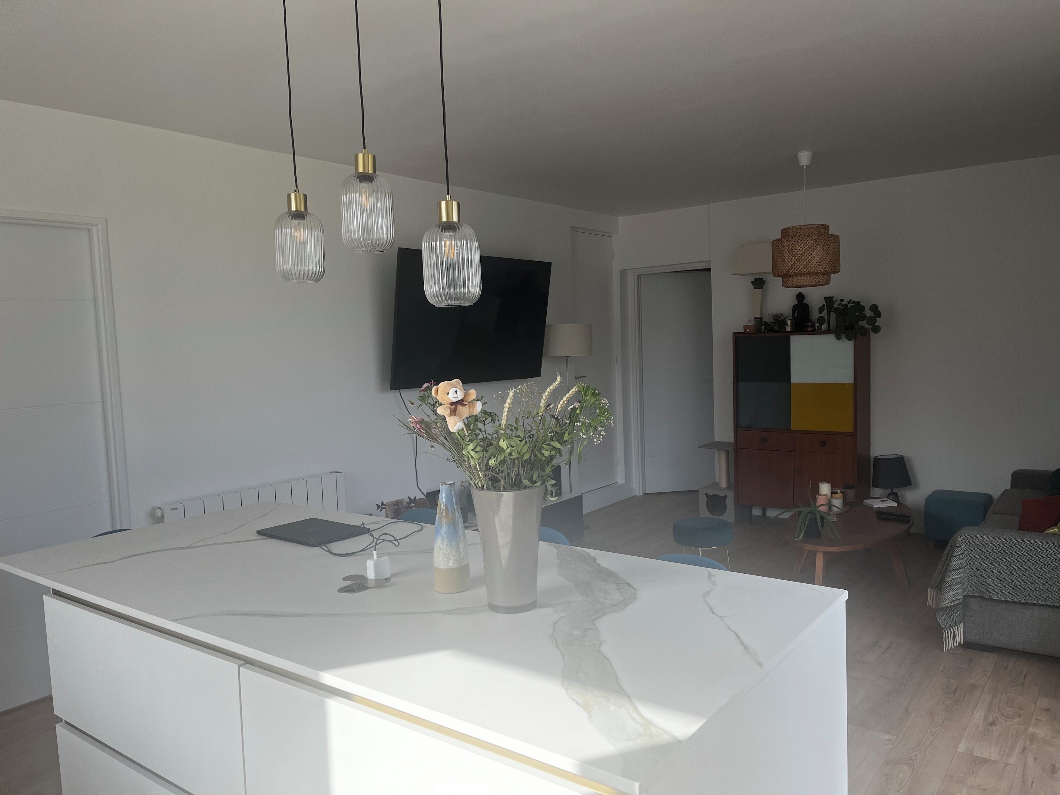Een moderne keuken met een marmeren eiland, hanglampen en een flatscreen televisie.
