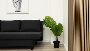 Un divano nero, una pianta verde grande e un pannello di legno verticale.