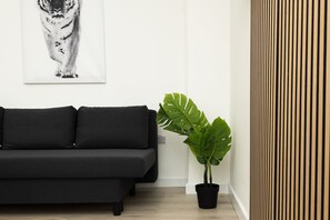 A black sofa, a large green plant, and a vertical wooden panel.