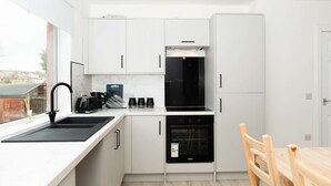 Una cucina moderna con mobili bianchi, un lavello nero e un tavolo da pranzo in legno.