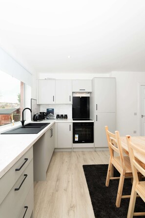 A modern kitchen with white cabinets, a black sink, and a wooden dining table.