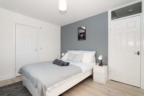 A bedroom with a bed, bedside tables, a nightstand, a grey wall, and a door.