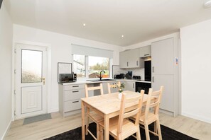 A modern kitchen with white cabinets, a wooden dining table, and a black rug.