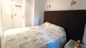 A bedroom with a bed, a nightstand, a wall-mounted lamp, and a door. - REF DOLOS BY PALMES D OR PROPERTIES (Cannes)