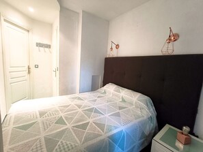 A bedroom with a bed, a nightstand, a wall-mounted lamp, and a door. - REF DOLOS BY PALMES D OR PROPERTIES (Cannes)