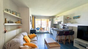A living room with a sofa, a coffee table, and a TV. There is a kitchen area with a microwave and a dining table. - REF DOLOS BY PALMES D OR PROPERTIES (Cannes)
