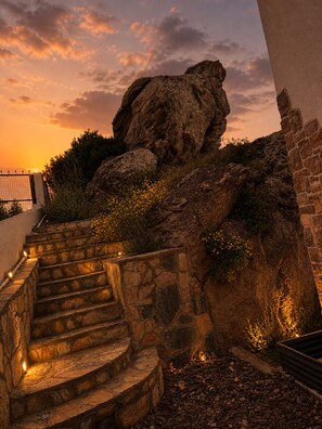 Eine Steintreppe führt zu einer Felsformation, im Hintergrund ein Sonnenuntergang.