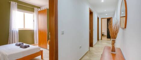 A hotel room with a bed, a bedside table, a mirror, and a hallway leading to another room.