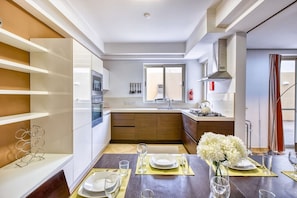 A modern kitchen with built-in appliances, a dining area set for four, and a view of the outside. - Serafina of Highgrove – 3BR Patio Home with BBQ (Swieqi)
