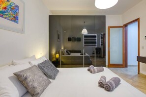 A modern hotel room with a large bed, a mirror, a sofa, and a view of the adjacent room. - Serafina of Highgrove – 3BR Patio Home with BBQ (Swieqi)