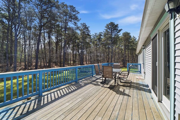 A wooden deck with a blue railing, a table with chairs, and a view of a forest.