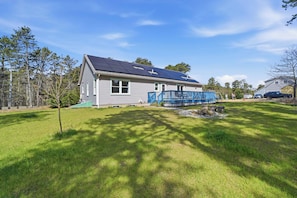 A house with solar panels, a fenced yard, and a small tree.