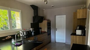Cozinha moderna com ilha central, cadeiras de madeira, forno embutido e vista para o verde lá fora.