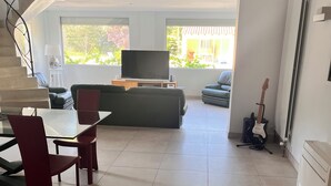 Sala de estar moderna com televisão, sofá, mesa de jantar, cadeiras e um violão.