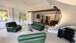 Uma sala de estar espaçosa com um sofá de couro verde, uma mesa de centro de vidro e uma escada que dá acesso a outro nível.