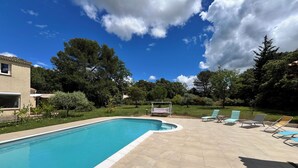 Piscina com deck ladrilhado, rodeada por vegetação e árvores.