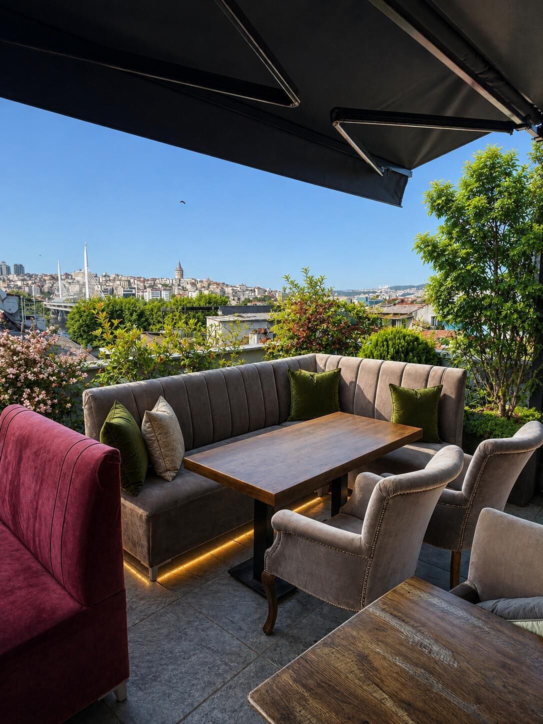 Terraza en la azotea con sofá, sillas y una mesa, con vistas a un paisaje urbano.