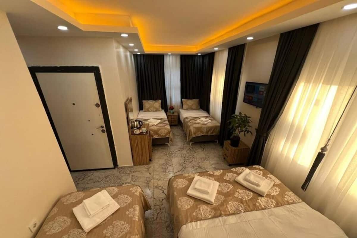 Quarto de hotel com duas camas, um espaço de estar pequeno, uma porta, uma televisão e uma planta.