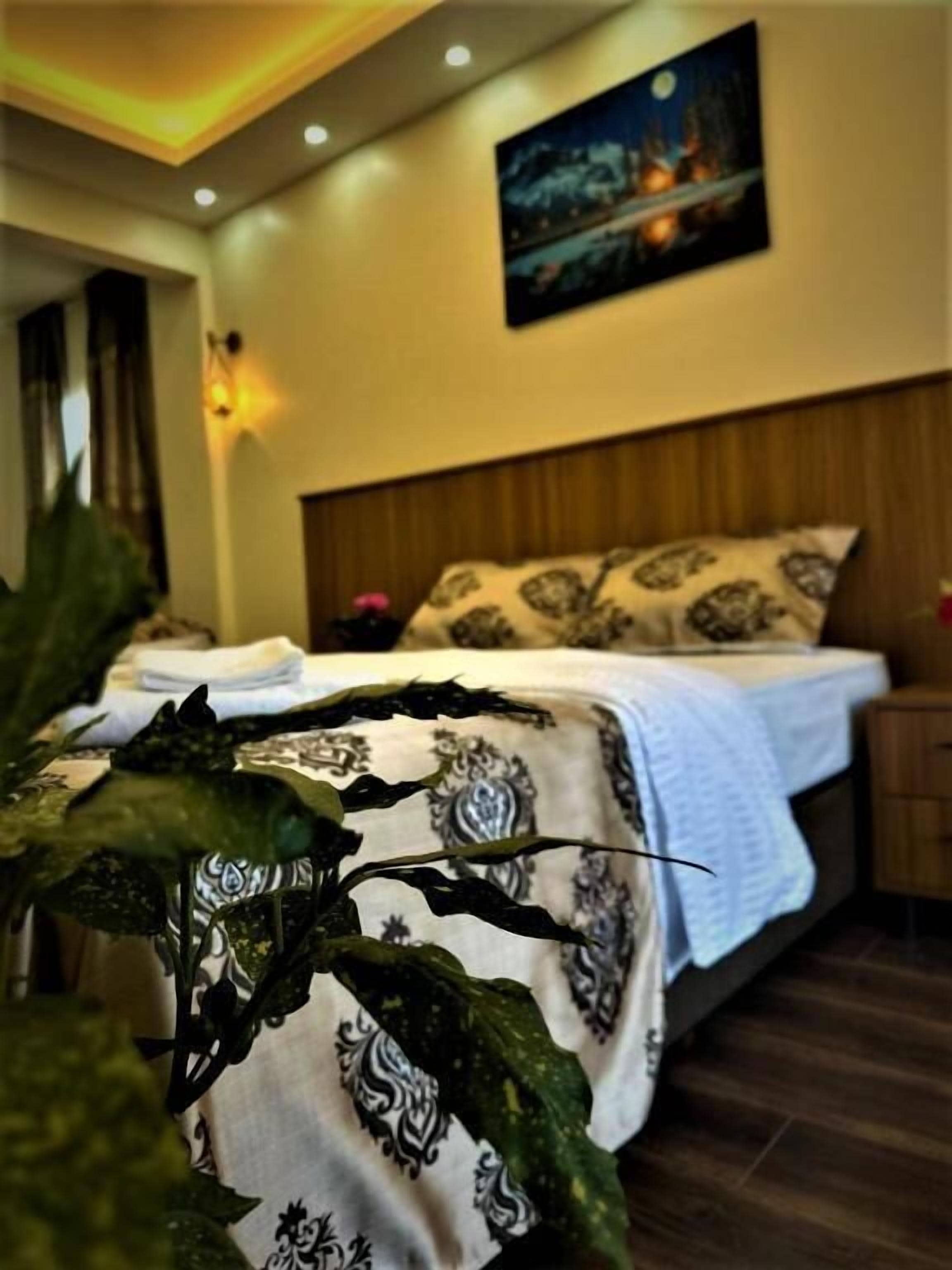 A bedroom with a bed, nightstand, wall art, and a potted plant.