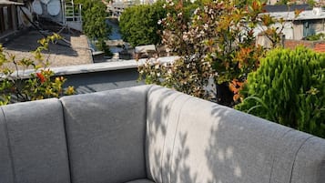 Une terrasse sur le toit avec un canapé gris, un téléphone intelligent posé sur le siège, et une vue sur le paysage urbain.