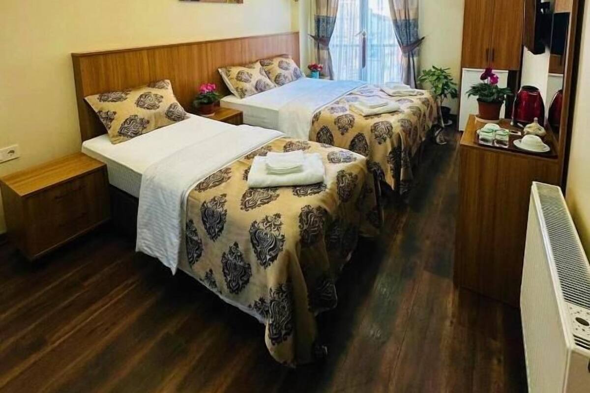 Quarto de hotel com duas camas, uma mesinha, televisão e luminária no teto.