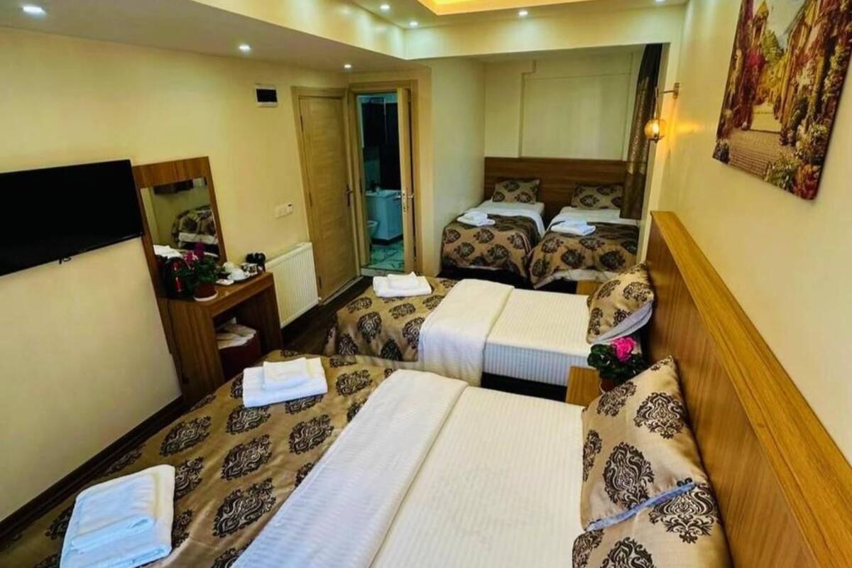Quarto de hotel com duas camas, televisão, espelho, mesa pequena e porta para um banheiro.