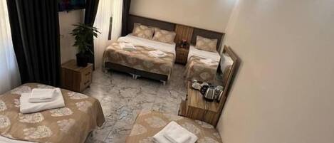 A hotel room with three beds, a TV, a plant, and a coffee machine.
