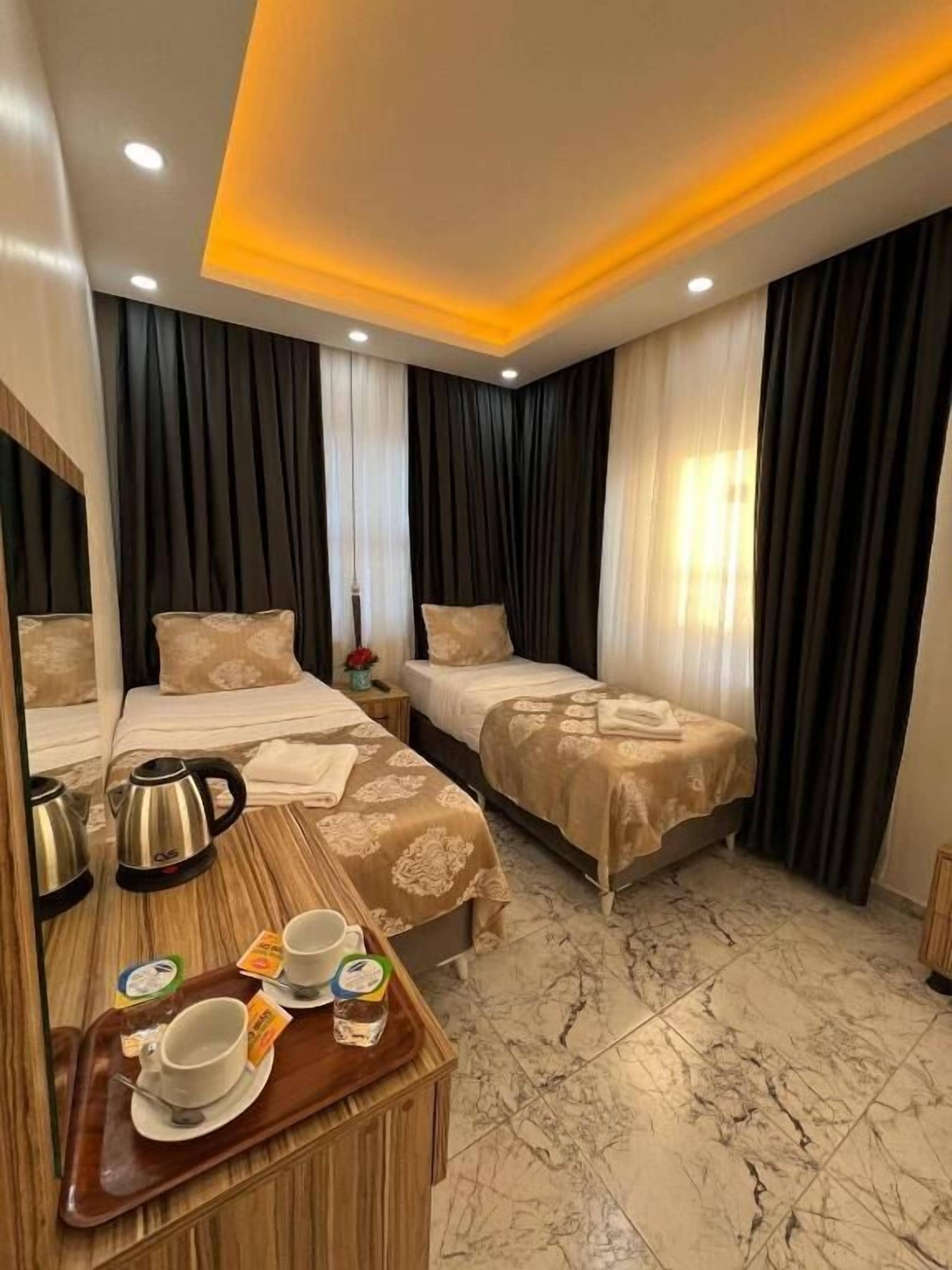Une chambre d’hôtel avec deux lits, une table de chevet en bois sur laquelle se trouve un plateau avec des articles pour le petit-déjeuner, et un sol en marbre.