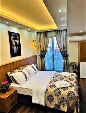Um quarto com cama, mesa de cabeceira, obra de arte na parede, janela com cortinas e ar condicionado.