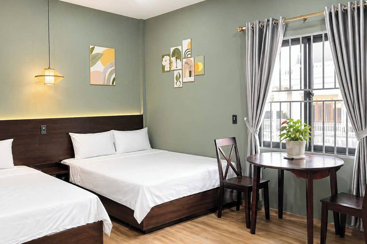 A hotel room with two beds, a round table with chairs, a potted plant, and artwork on the walls.