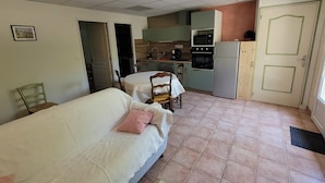 Ett kompakt bostadsutrymme med en soffa, ett matbord, ett köksområde med vitvaror och en dörr.