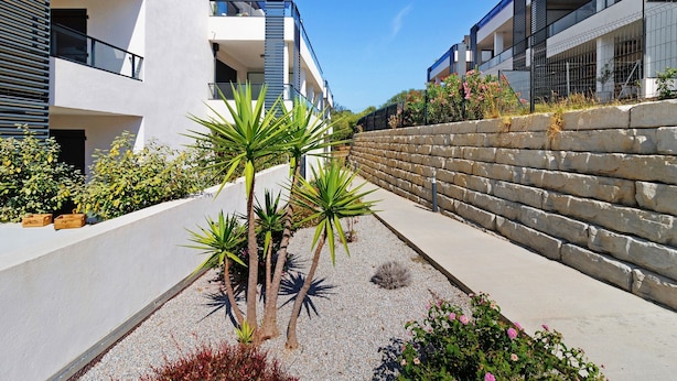 Un bâtiment moderne doté de balcons, d’un mur de soutènement en pierre et d’une grande variété de plantes.