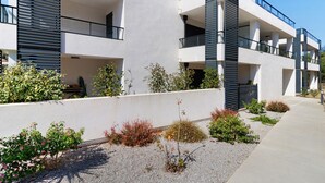 Un edificio moderno de varios pisos con balcones, un camino de grava y diversos arbustos.