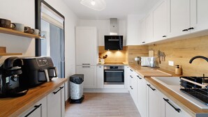 Una cocina moderna con armarios blancos, encimera de madera, cafetera y horno empotrado.