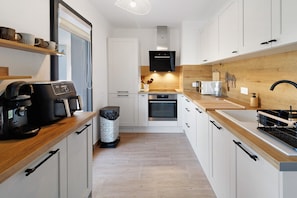Una cocina moderna con armarios blancos, encimera de madera, cafetera y horno empotrado.
