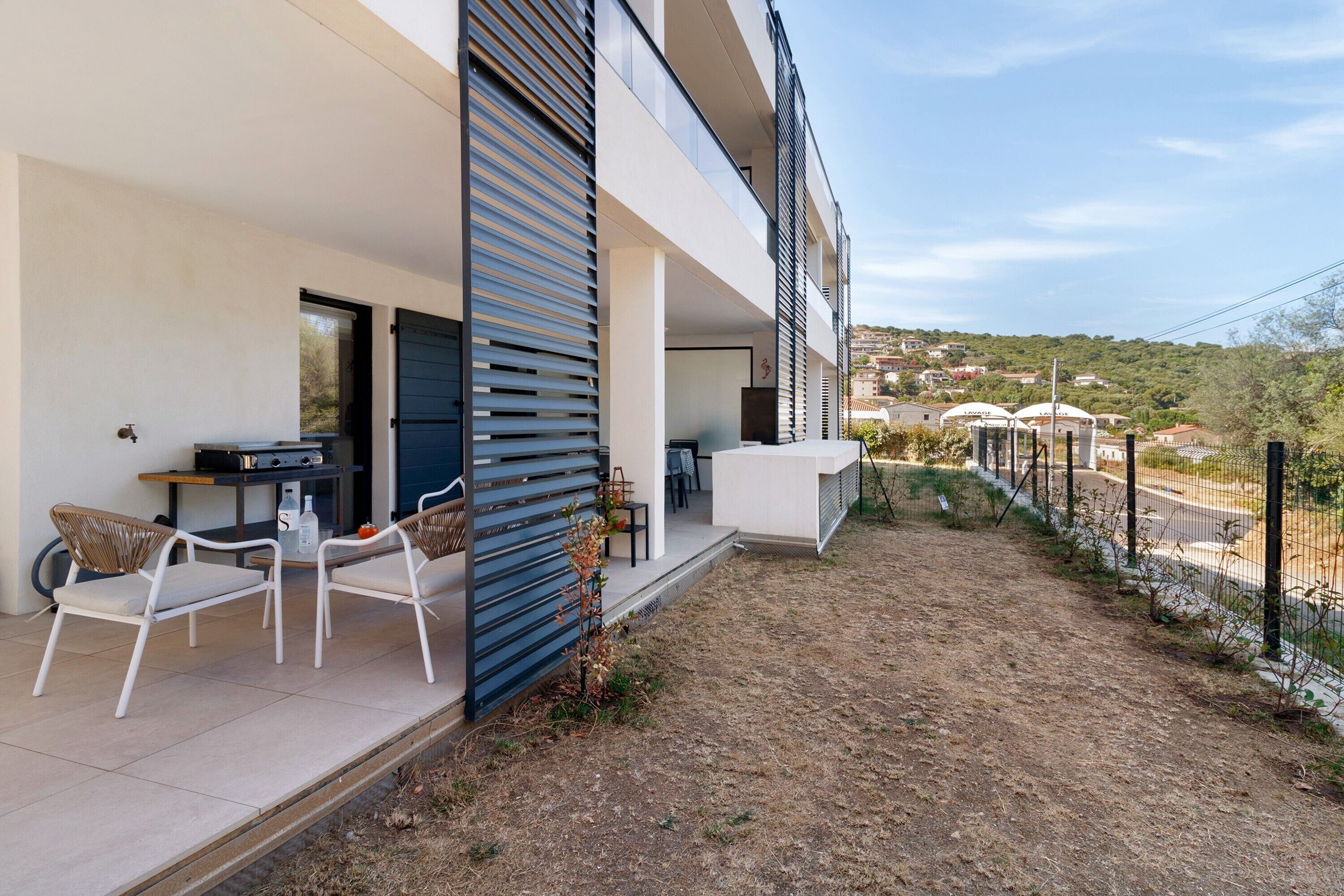 Un bâtiment moderne doté d’un espace extérieur aménagé avec une zone de sièges couverte, une petite table et des chaises.