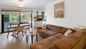 Una sala de estar con un sofá marrón, una mesa de comedor con sillas y una cocina al fondo.
