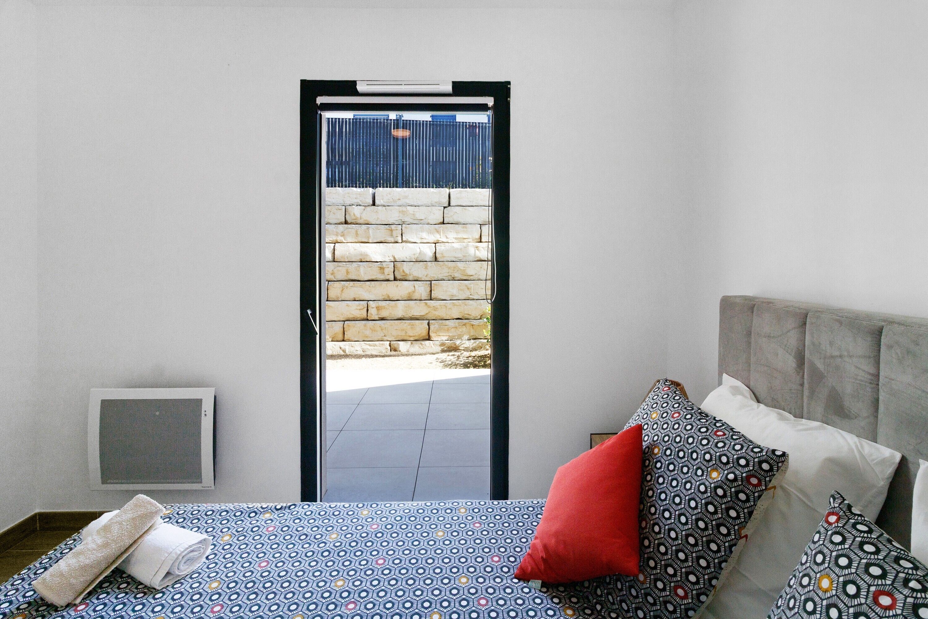 A bedroom with a bed, pillows, a towel, a heater, and a door leading to an outdoor area.