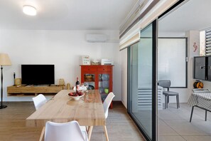 Ein modernes Wohnzimmer mit einem Holzesstisch, weißen Stühlen, einem Flachbildfernseher, einem roten Schrank und einer Glastür zum Balkon.