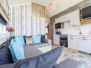 A modern interior with a sofa, patterned cushions, a kitchen with white cabinets, and a hanging light fixture. - Posh Pod (Cemaes Bay)