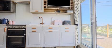 A modern kitchen with white cabinets, a built-in oven, a sink with a copper faucet, and a television mounted above the counter.