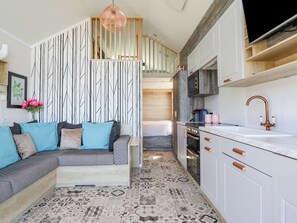 A compact kitchen with white cabinets, a copper faucet, and a patterned floor. - Posh Pod (Cemaes Bay)