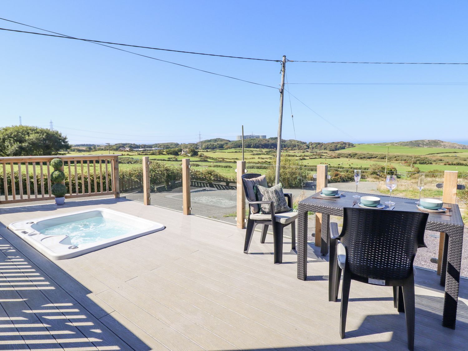 A patio with a hot tub, outdoor seating, and a scenic view of hills and fields.