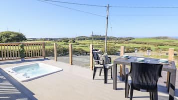 A patio with a hot tub, outdoor seating, and a scenic view of hills and fields.
