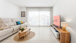 A modern living room with a sofa, a coffee table, a TV, and a lamp. - GuestReady-Sunny Modern Retreat in Mira (Mira)
